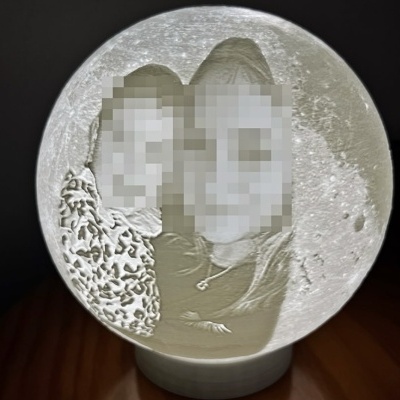 Lâmpada decorativa redonda com relevo da lua e imagem gravada de duas pessoas pixeladas.