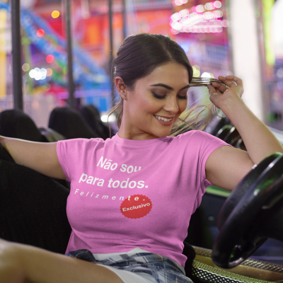 Mulher sorridente a usar t-shirt rosa com texto em branco, sentada num carro de diversão colorido.