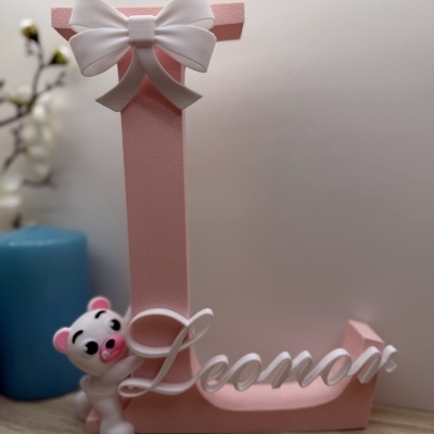 Letra decorativa cor-de-rosa com arco branco e ursinho junto com nome Leonor.