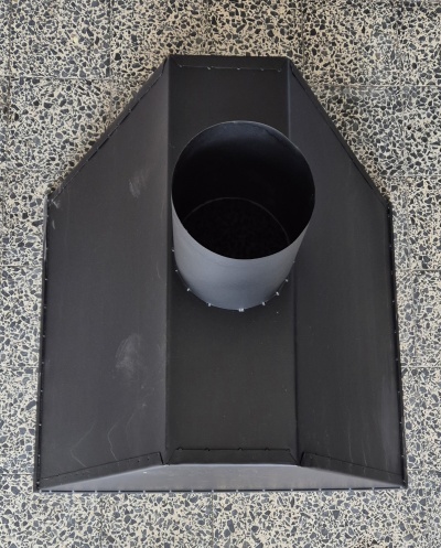 Chaminé metálica preta com tubo central sobre chão cinza