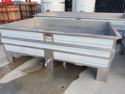 Tanque industrial em inox com torneiras e etiqueta num ambiente de armazém