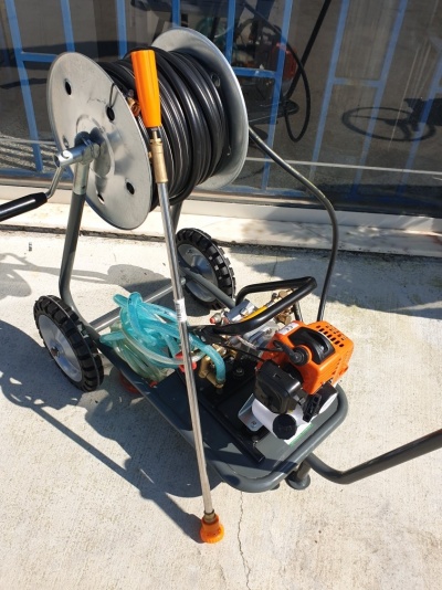 Carrinho com mangueira enrolada, bomba motorizada laranja e rodas.