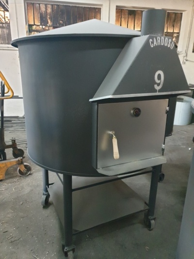 Fogão industrial cinzento com porta e inscrições na chaminé numa oficina