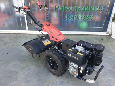 Motoenxada metálica preta e vermelha com motor a gasolina, em pavimento, junto a porta de vidro com texto 'Pulverizadores Cardoso'.