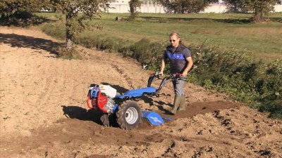 Trator de solo azul a arar terra com operador em campo rural
