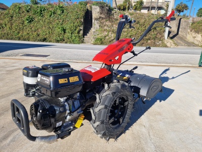 Motoenxada vermelha e preta com motor a gasolina em cimento