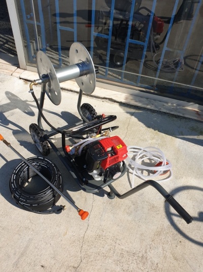 Máquina pulverizadora com motor vermelho e carretel metálico em chão de cimento