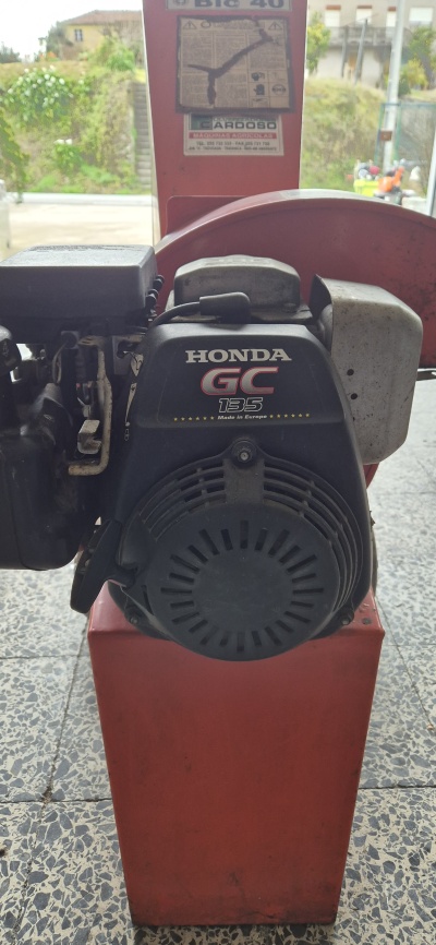 Motor Honda GC 135 preto montado numa caixa vermelha, em chão de azulejos cinzentos.