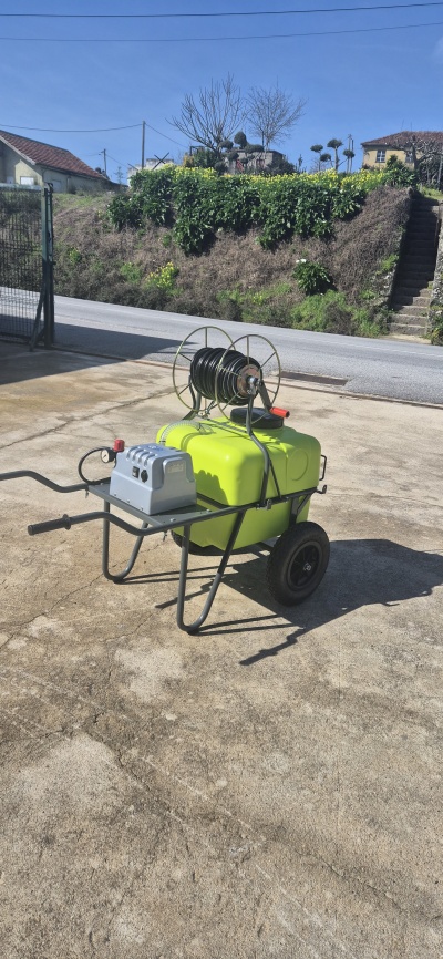 Pulverizador manual verde com carreto de mangueira e estrutura metálica sobre chão de cimento