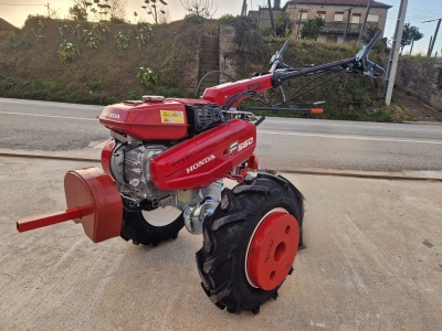 Motoenxada Honda F-560 vermelha com pneus pretos numa superfície clara ao ar livre