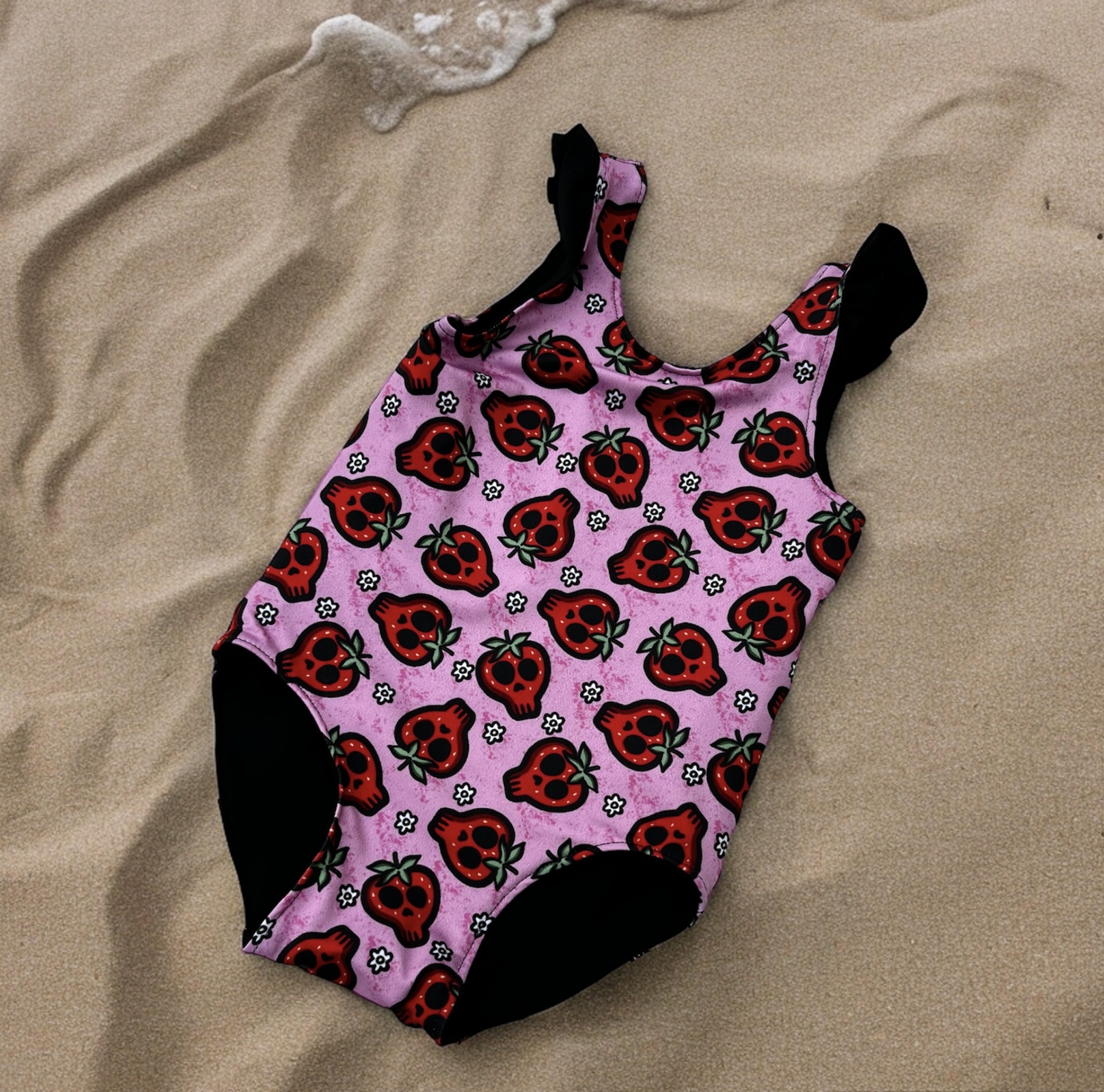 Fato de banho rosa com padrão de maçãs vermelhas e pretas na areia