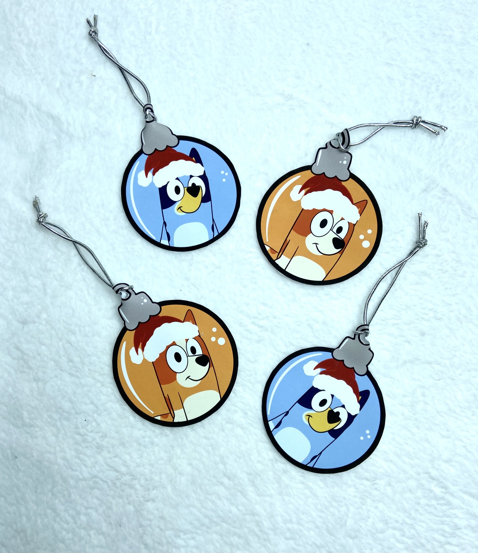 Quatro ornamentos de natal redondos com personagens de desenho animado e gorros de natal, sobre fundo branco texturizado.
