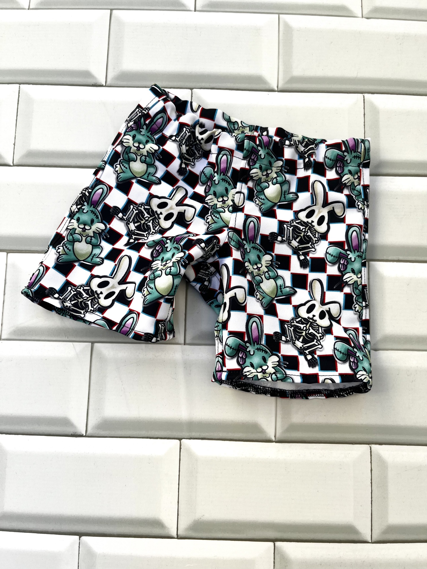Calções de criança com padrão de coelhos, crânios e aranhas sobre azulejos brancos