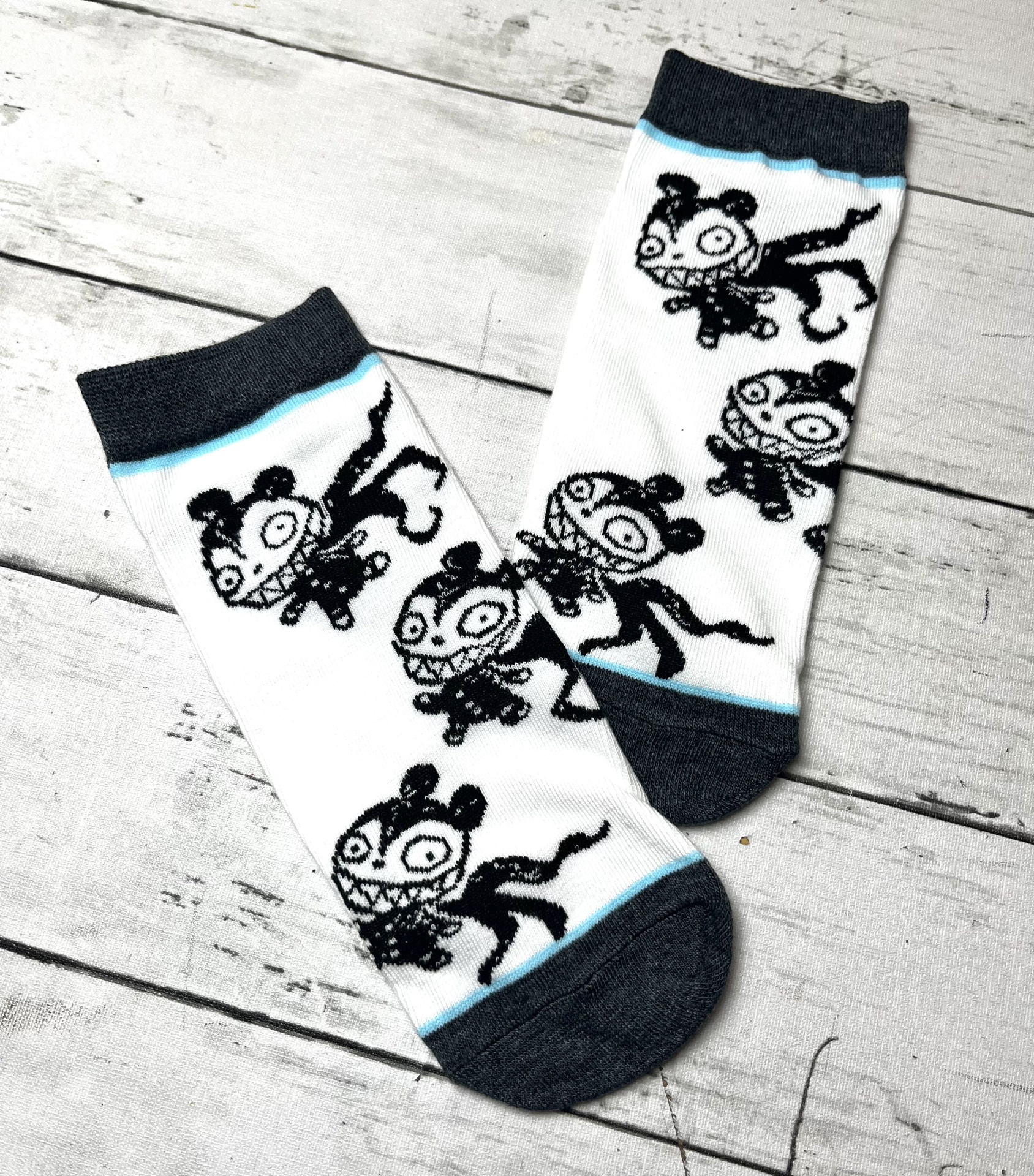 Meias brancas com desenhos pretos de personagens e detalhes cinzentos e azul claro.