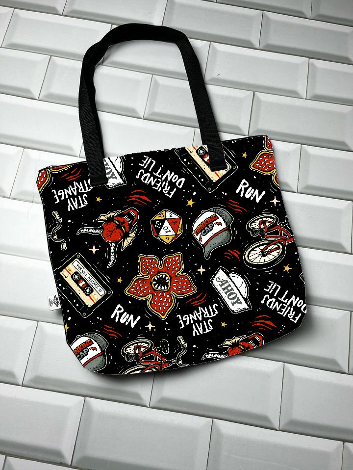 Mala de tecido preta com desenhos e frases coloridas e alças pretas sobre chão de azulejos brancos