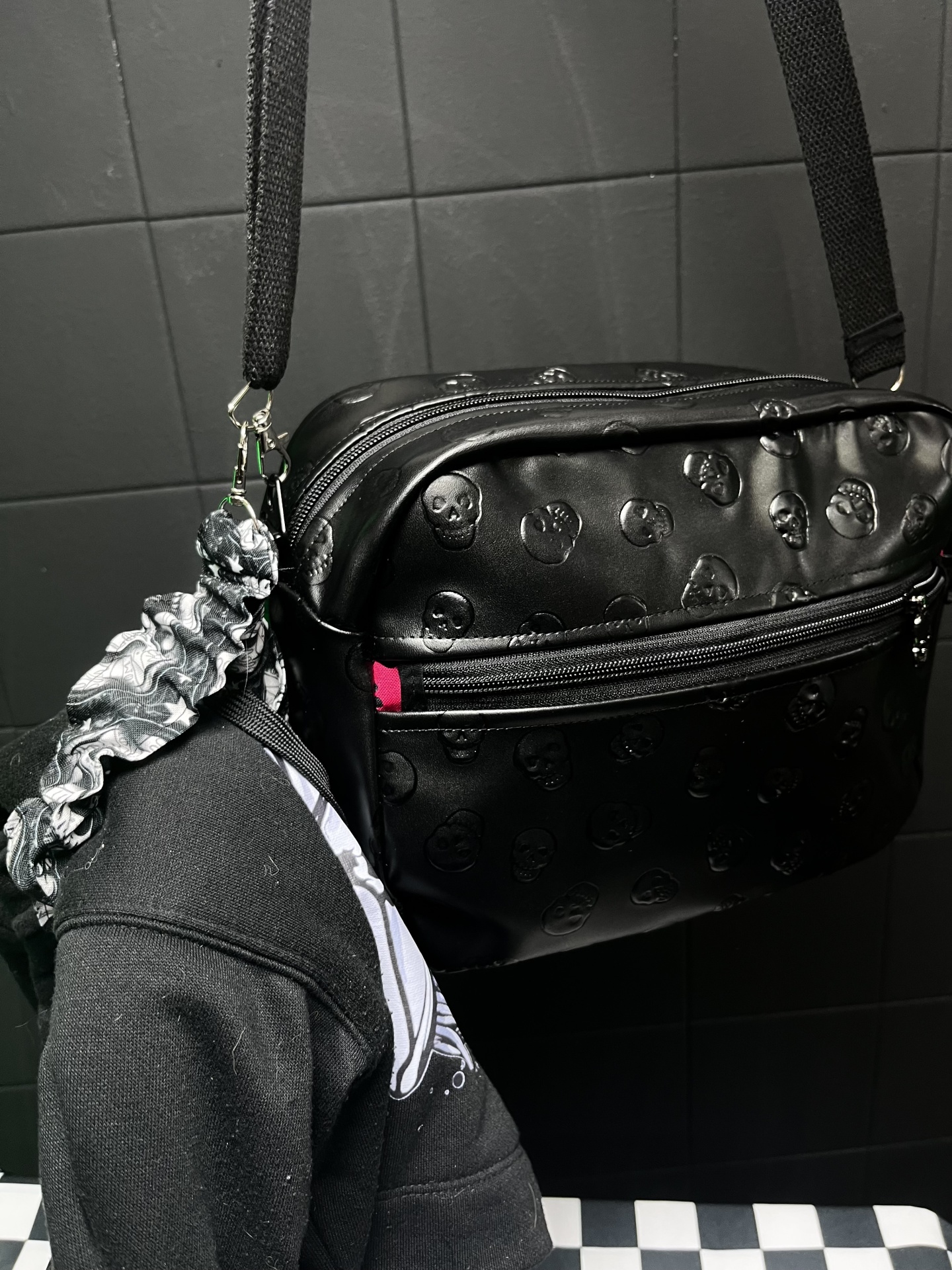 Mala preta com padrão de caveiras em relevo pendurada com roupa preta e fita de cabelo cinza