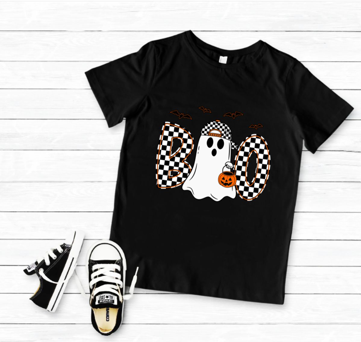 T-shirt preta infantil com estampa de fantasma de Halloween e ténis pretos e brancos ao lado.