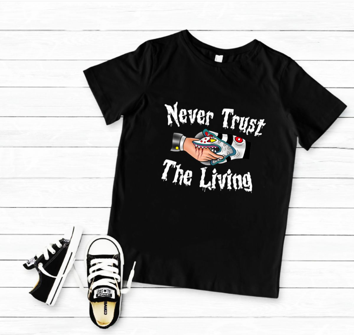 T-shirt preta com estampa colorida e texto com ténis infantis ao lado em fundo de madeira branca