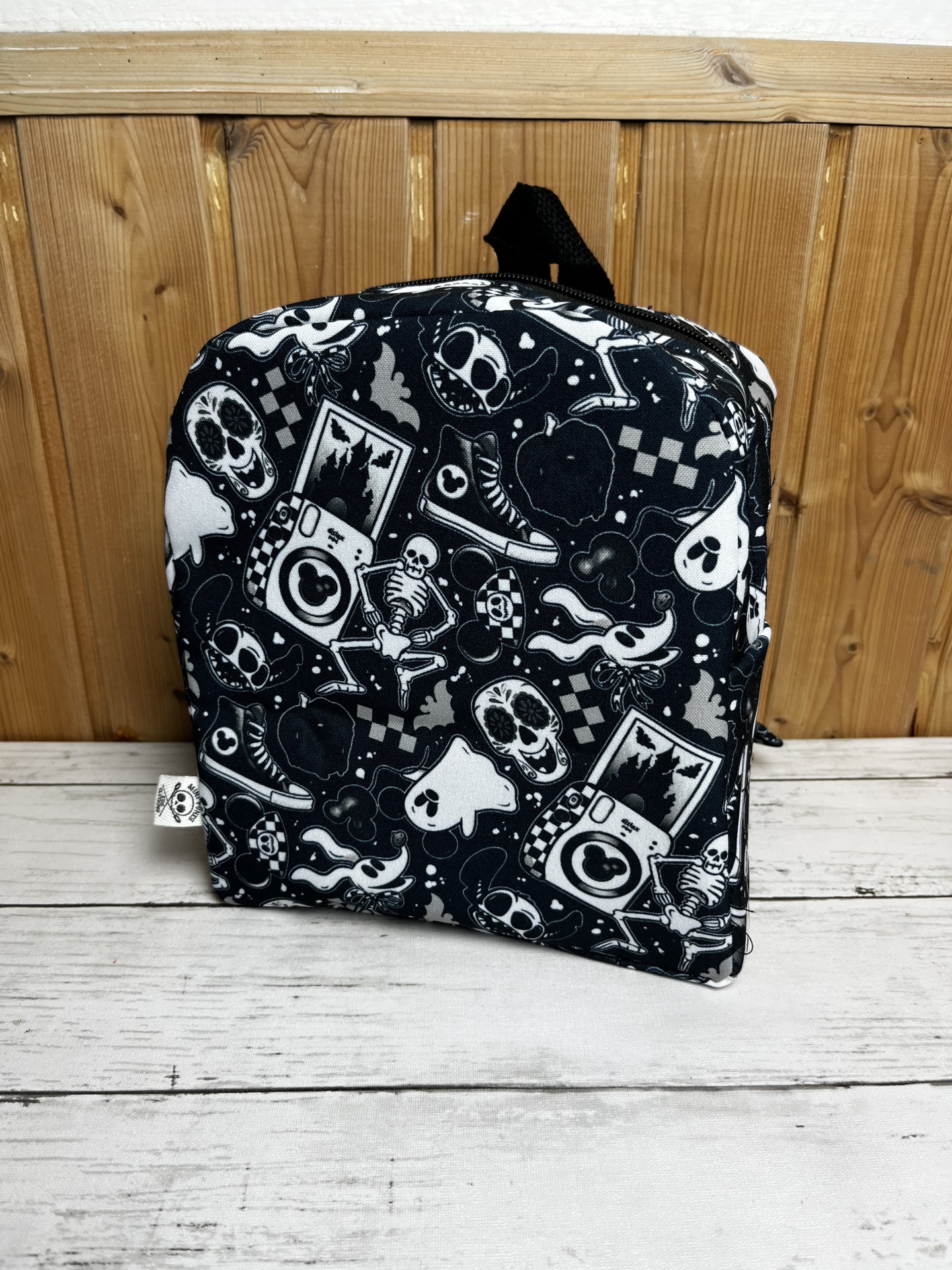 Mochila preta com estampado branco de caveiras, esqueletos e ícones diversos.