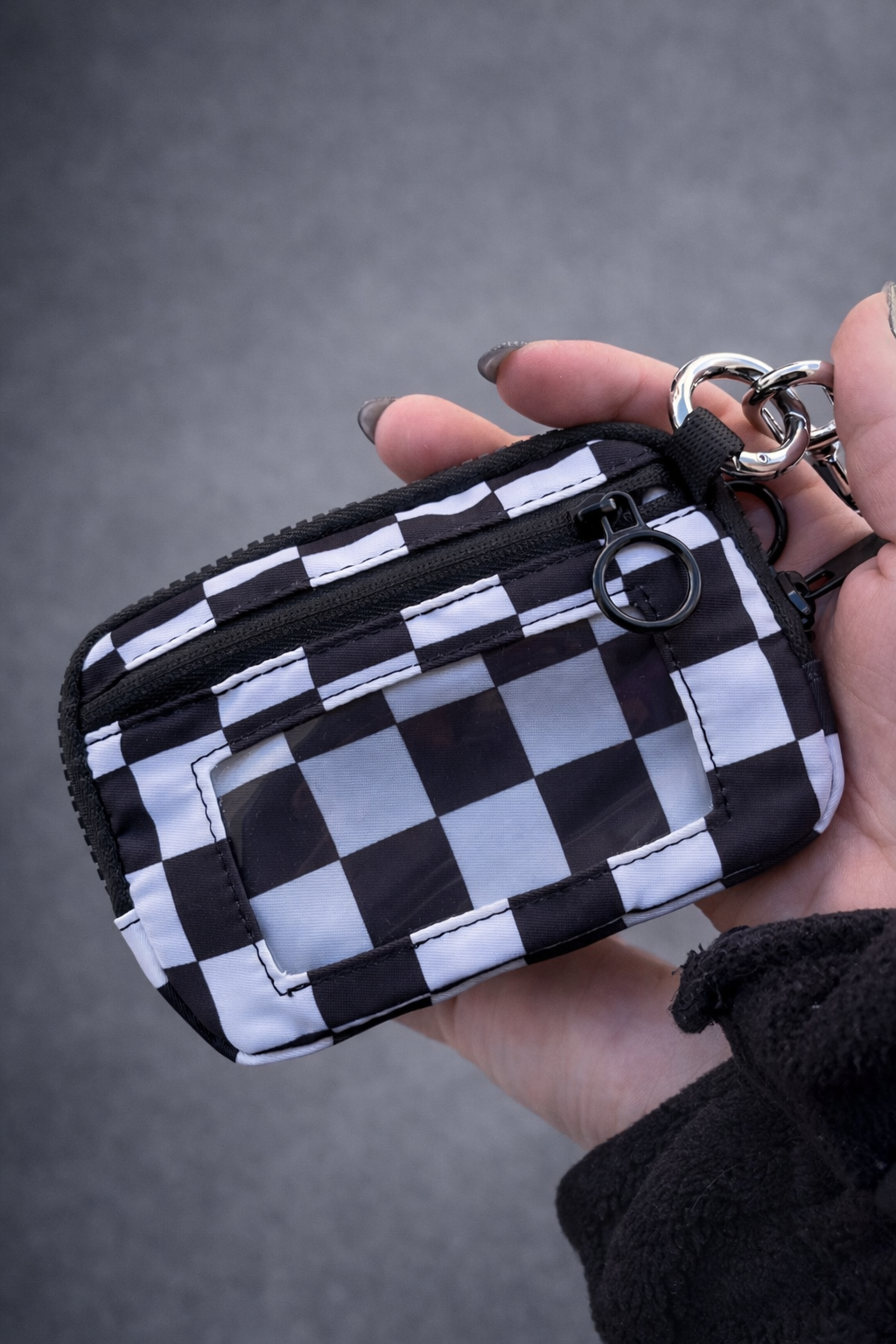 Carteira pequena preta e branca com padrão xadrez, fecho éclair e argola metálica.