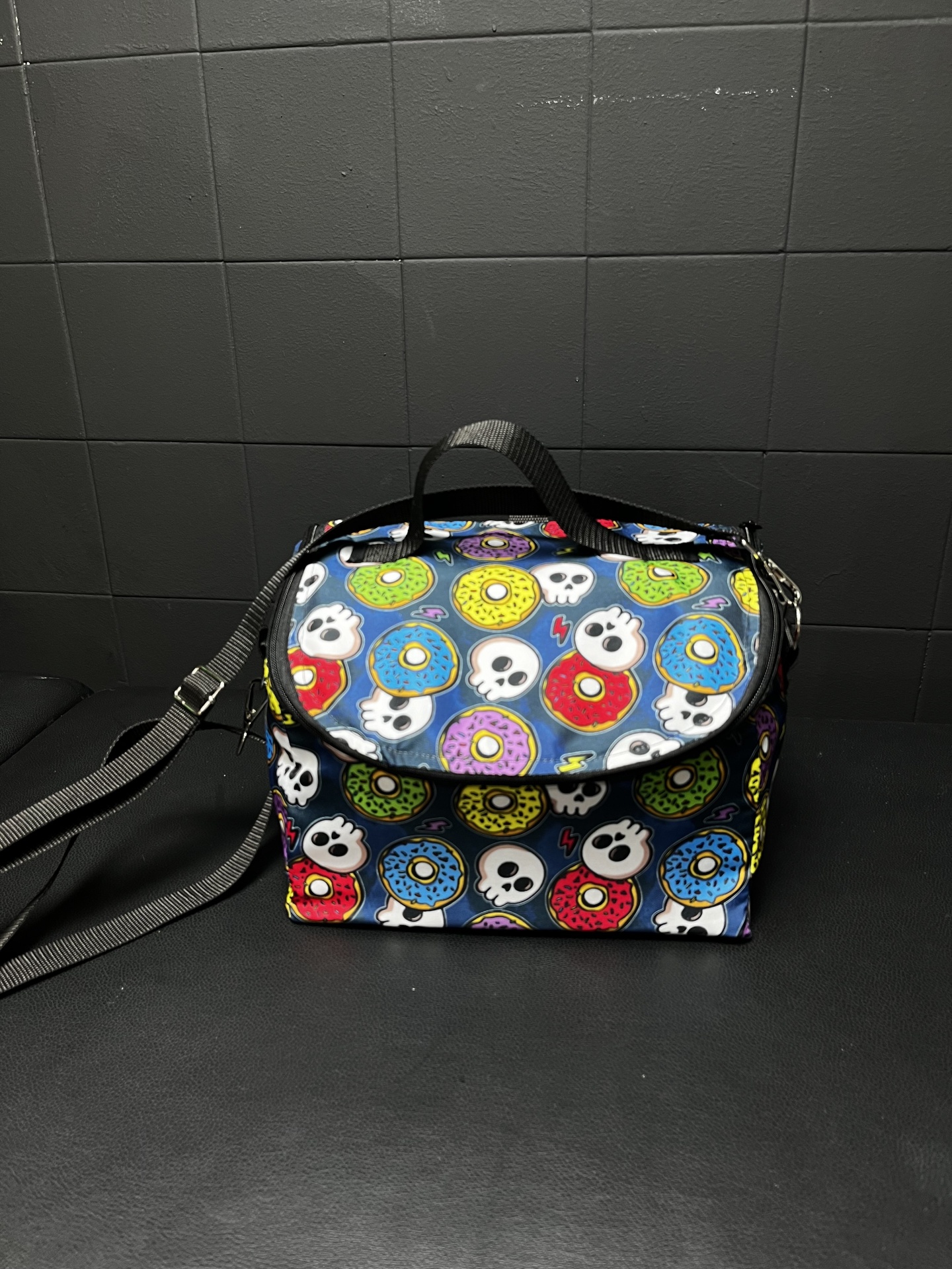 Bolsa pequena com padrão de donuts e caveiras, alça preta, fundo azul