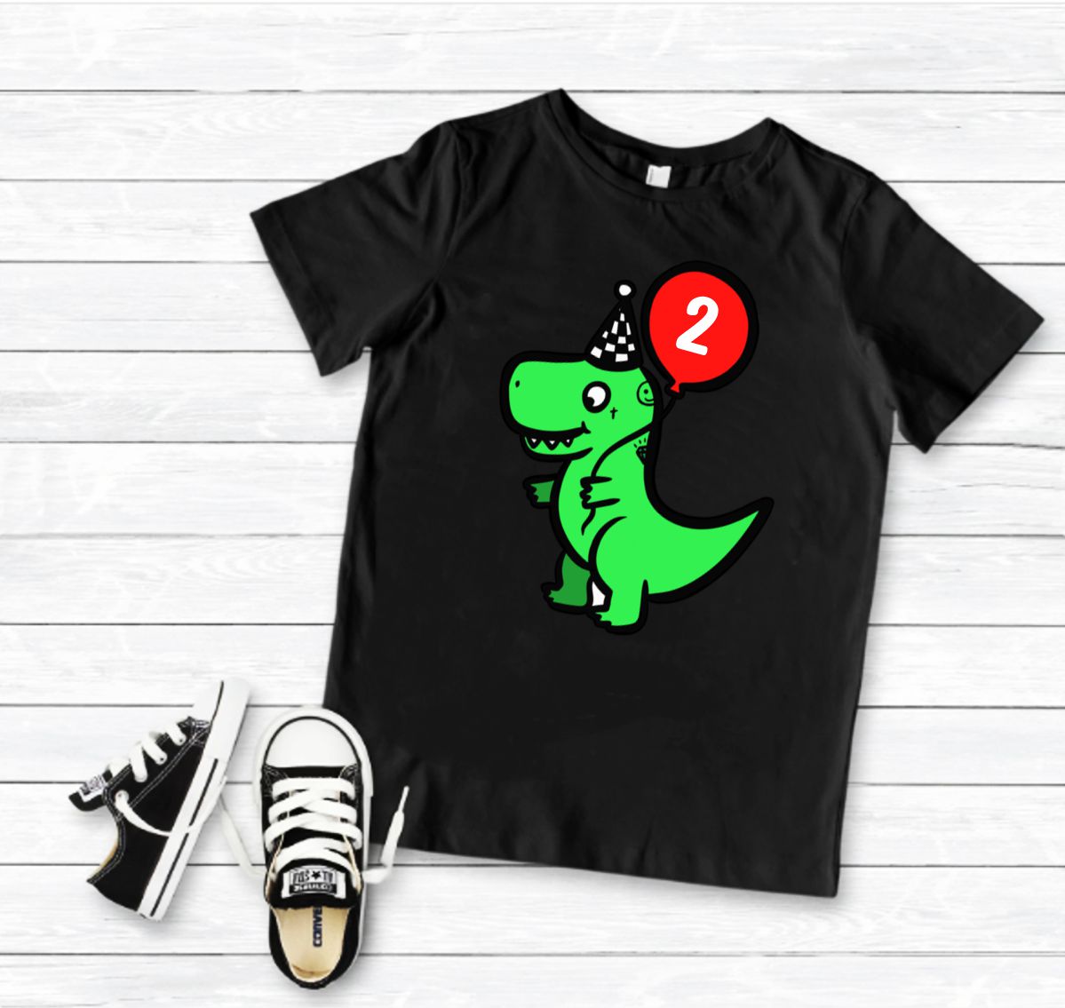 T-shirt preta com estampa de dinossauro verde e balão vermelho, com ténis infantis pretos e brancos ao lado