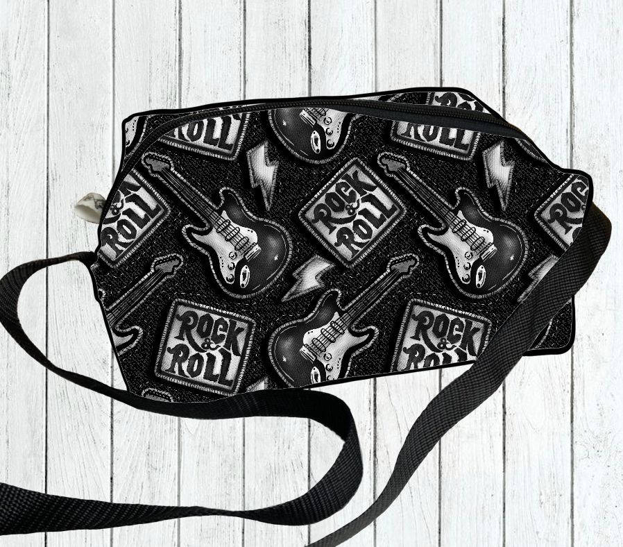 Mala preta com padrão de guitarras e texto 'ROCK & ROLL', alça preta, sobre fundo de madeira branca