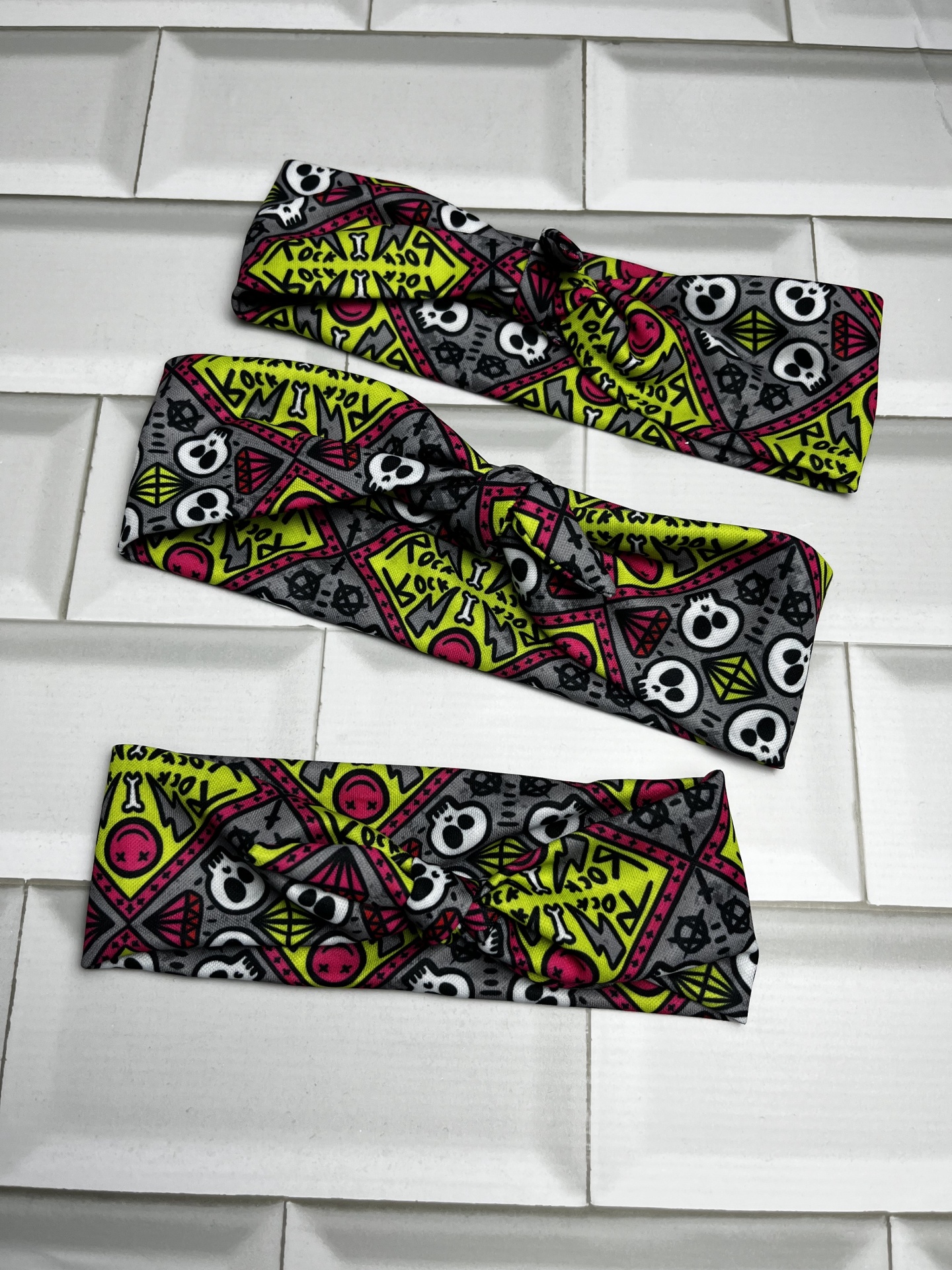 Três faixas de cabelo coloridas com estampado de caveiras e triângulos sobre azulejos brancos