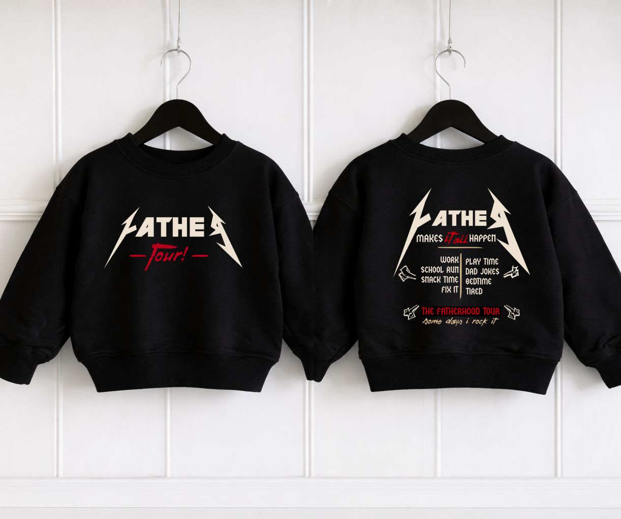 Dois sweatshirts pretos para criança, com estampas brancas e vermelhas, pendurados em cabides pretos contra parede branca.