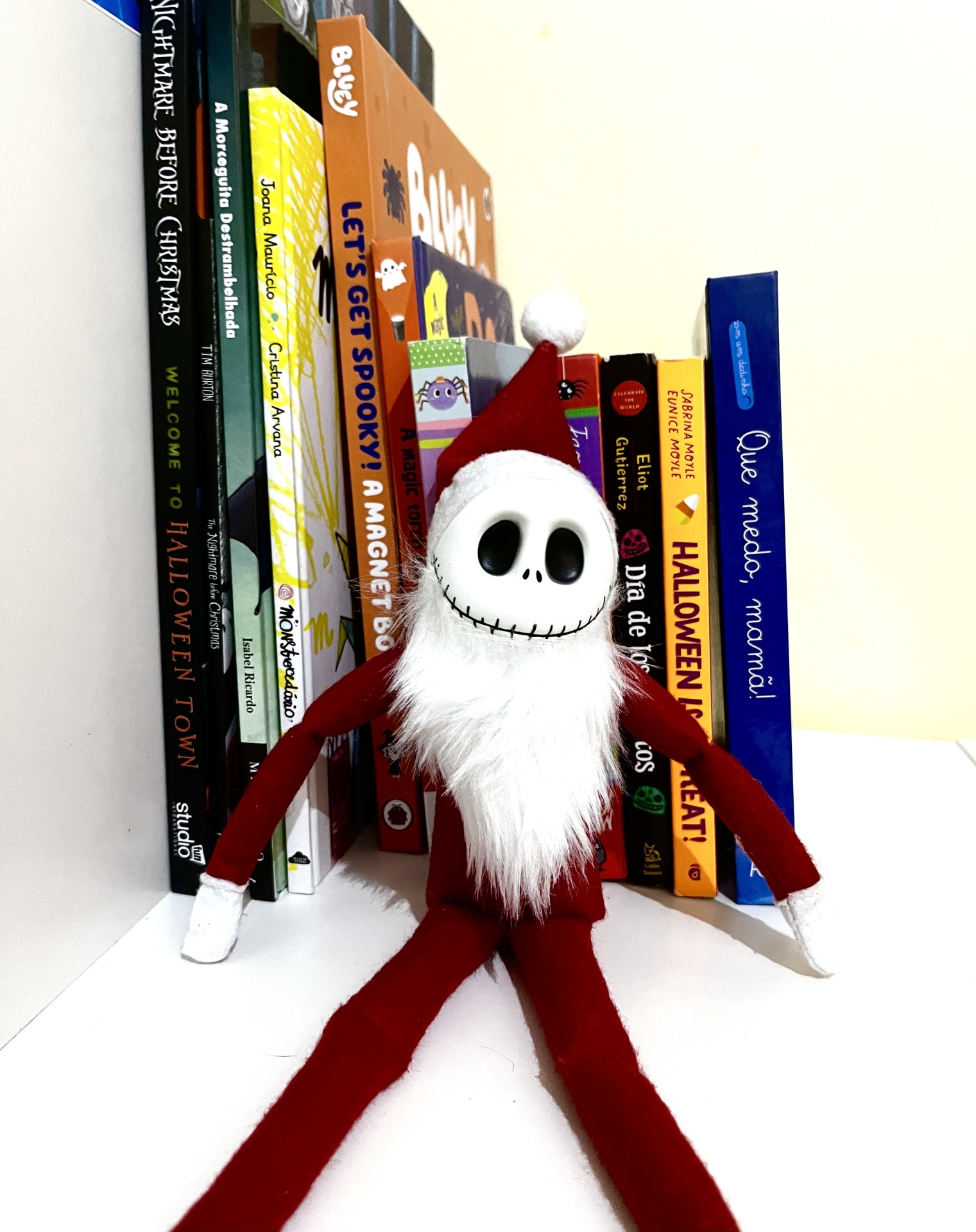 Boneco de pelúcia estilo Papai Noel com rosto branco e livros coloridos ao fundo
