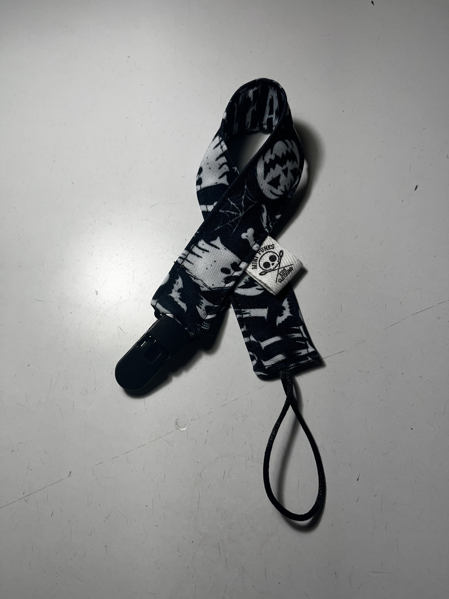 Prendedor de chupeta preto e branco com caveiras e teias de aranha