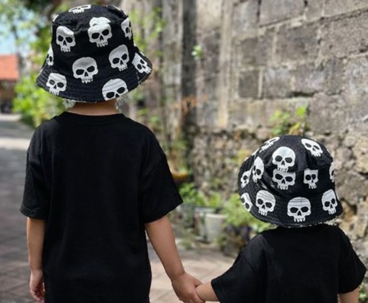 Crianças de costas com chapéus pretos de caveira e t-shirts pretas