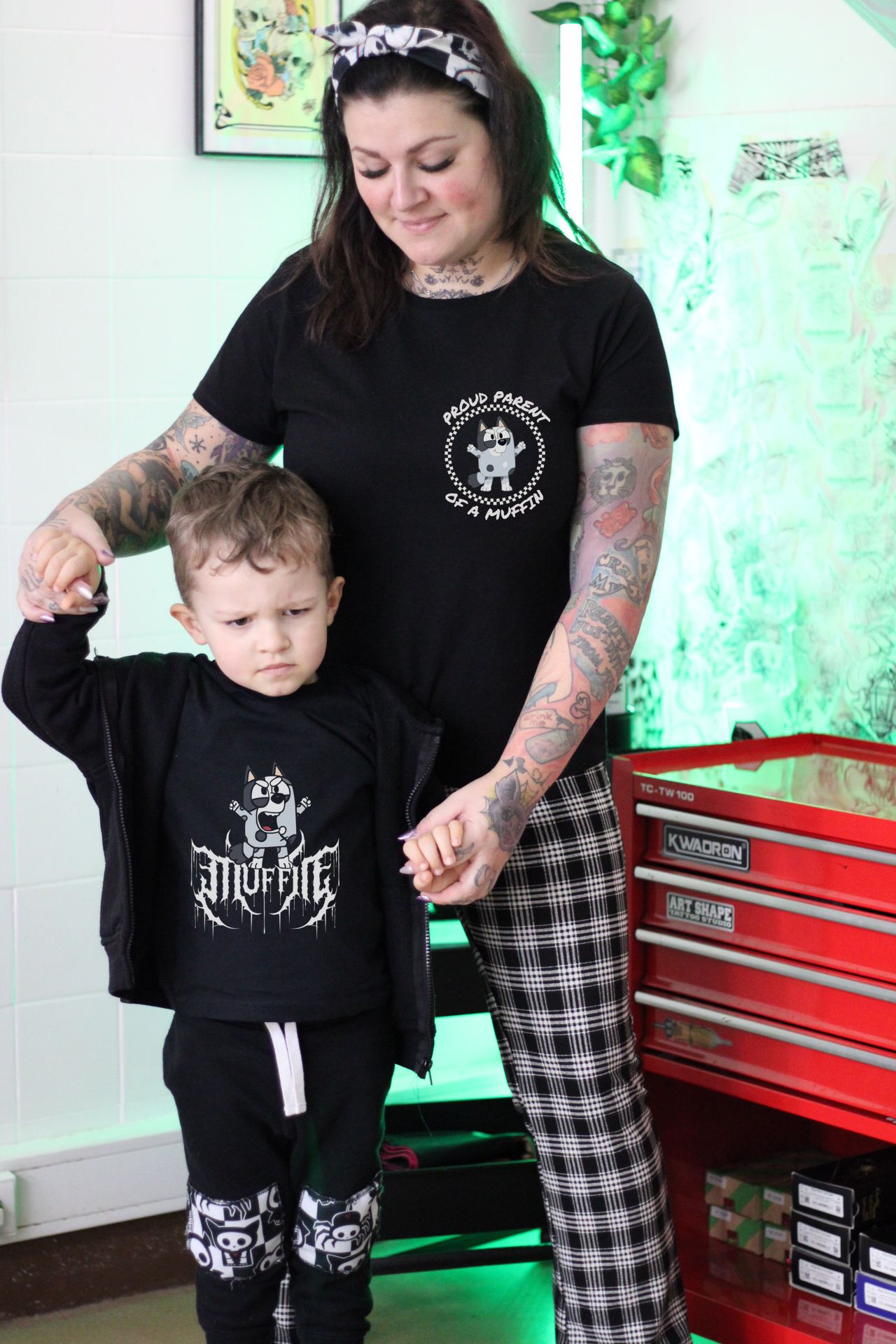 Mãe e criança com roupa preta, mãe com calças xadrez, junto a caixa de ferramentas vermelha.