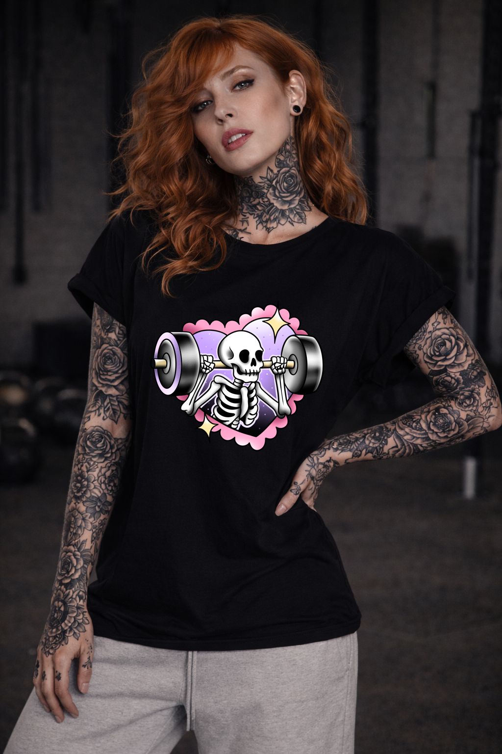 Mulher com t-shirt preta de esqueleto a levantar halteres, tatuagens florais no pescoço e braços.