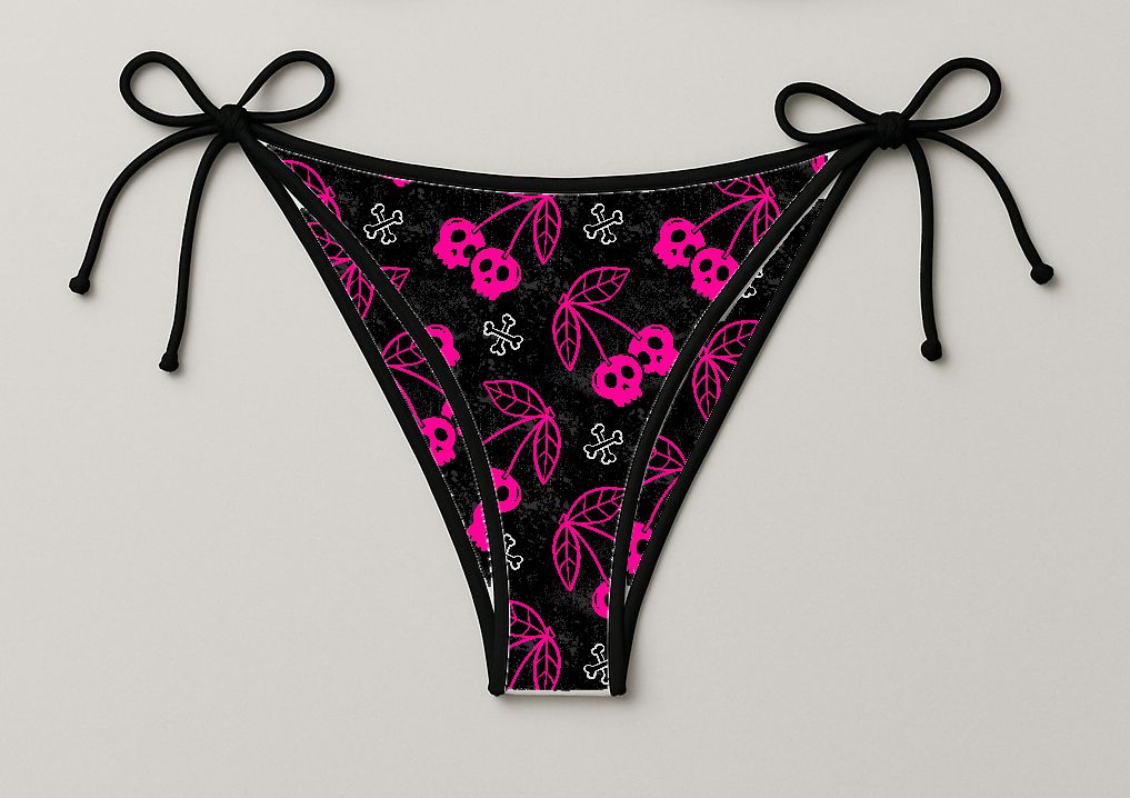 Cueca de banho tanga preta com padrão de caveiras rosas e ossos brancos, com laços pretos nas laterais.