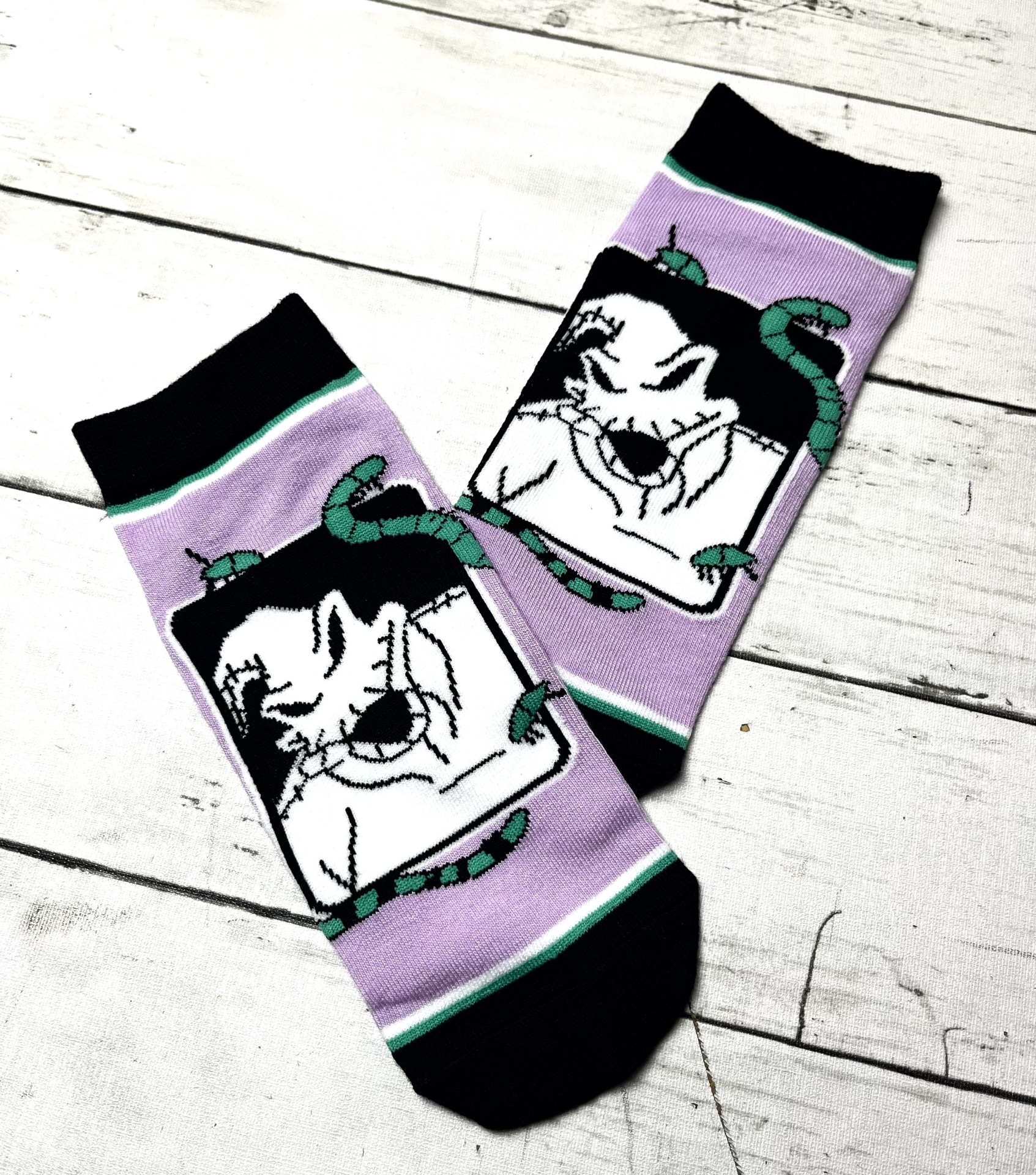 Meias lilás com ponteiras e punhos pretos e desenho de rosto branco com cobras verdes.