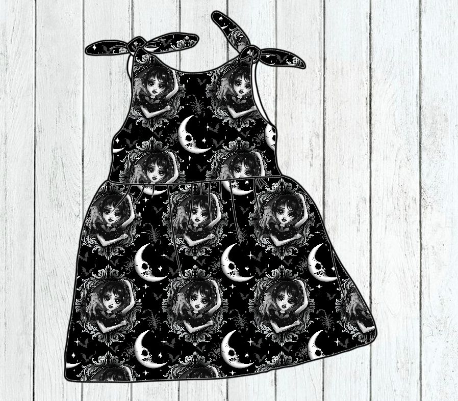 Vestido infantil preto e branco com padrão de rostos femininos, luas e flores, alças com laço