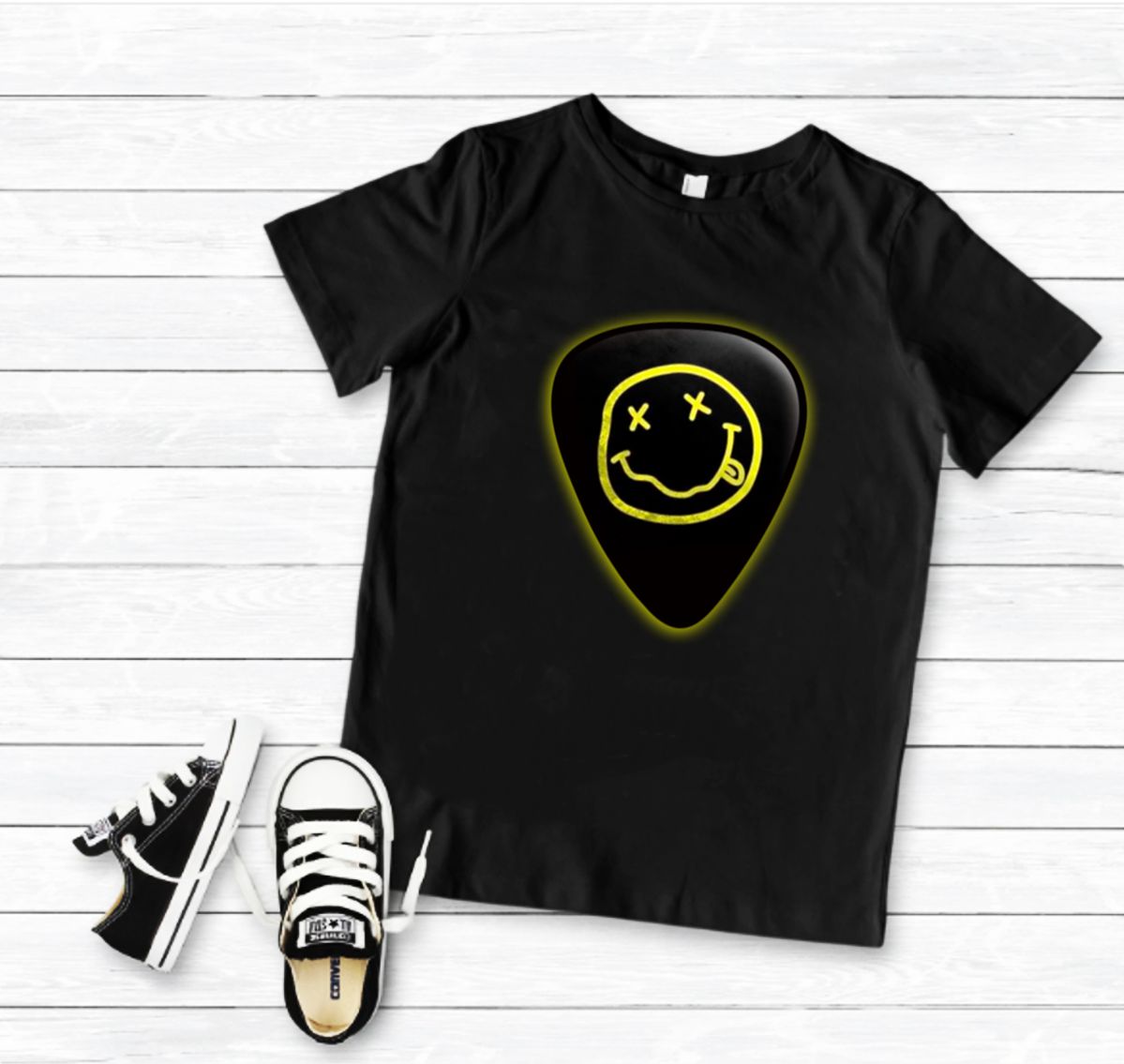 T-shirt preta com estampa de palheta e rosto sorridente, com ténis pretos ao lado, sobre chão de madeira branca
