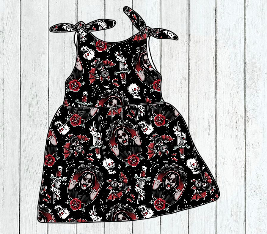 Vestido infantil preto com padrão de caveiras, rosas e retratos em fundo branco de madeira