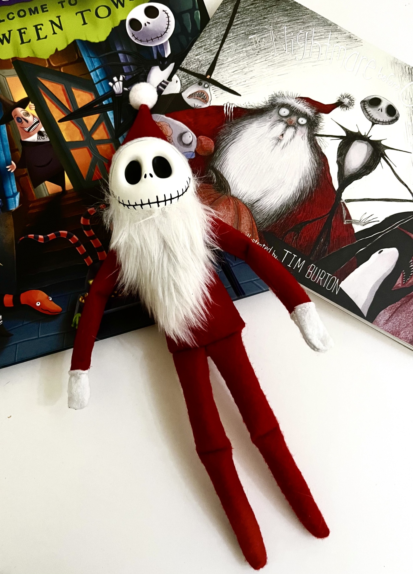 Boneco de pelúcia com roupa vermelha e cabeça de caveira ao lado de um livro ilustrado.