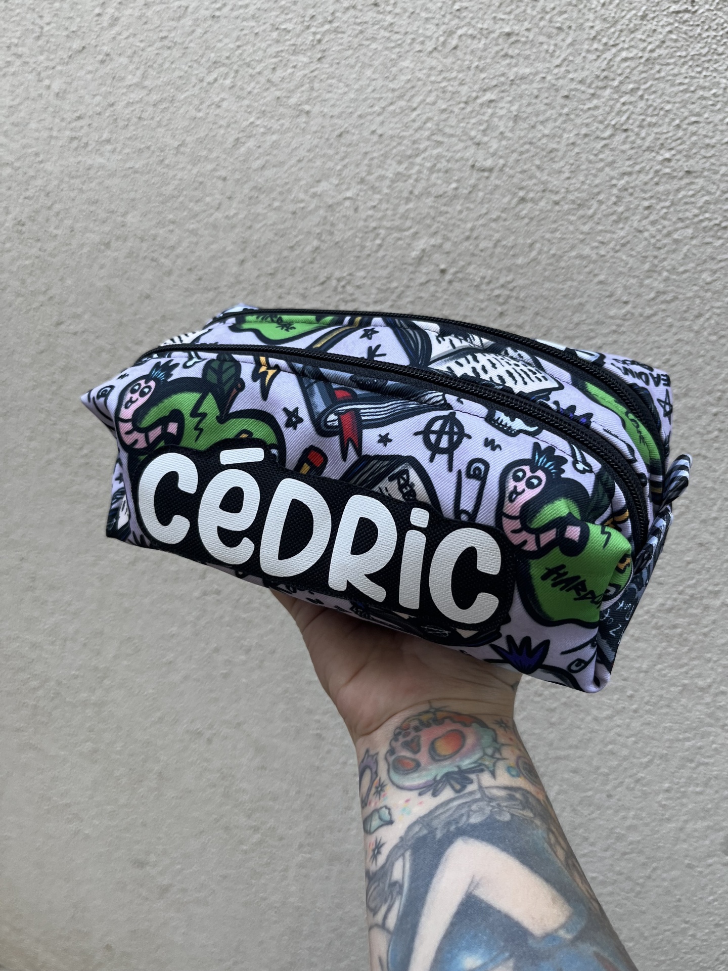 Bolsa com padrão colorido e o texto CÉDRIC em branco sobre fundo preto