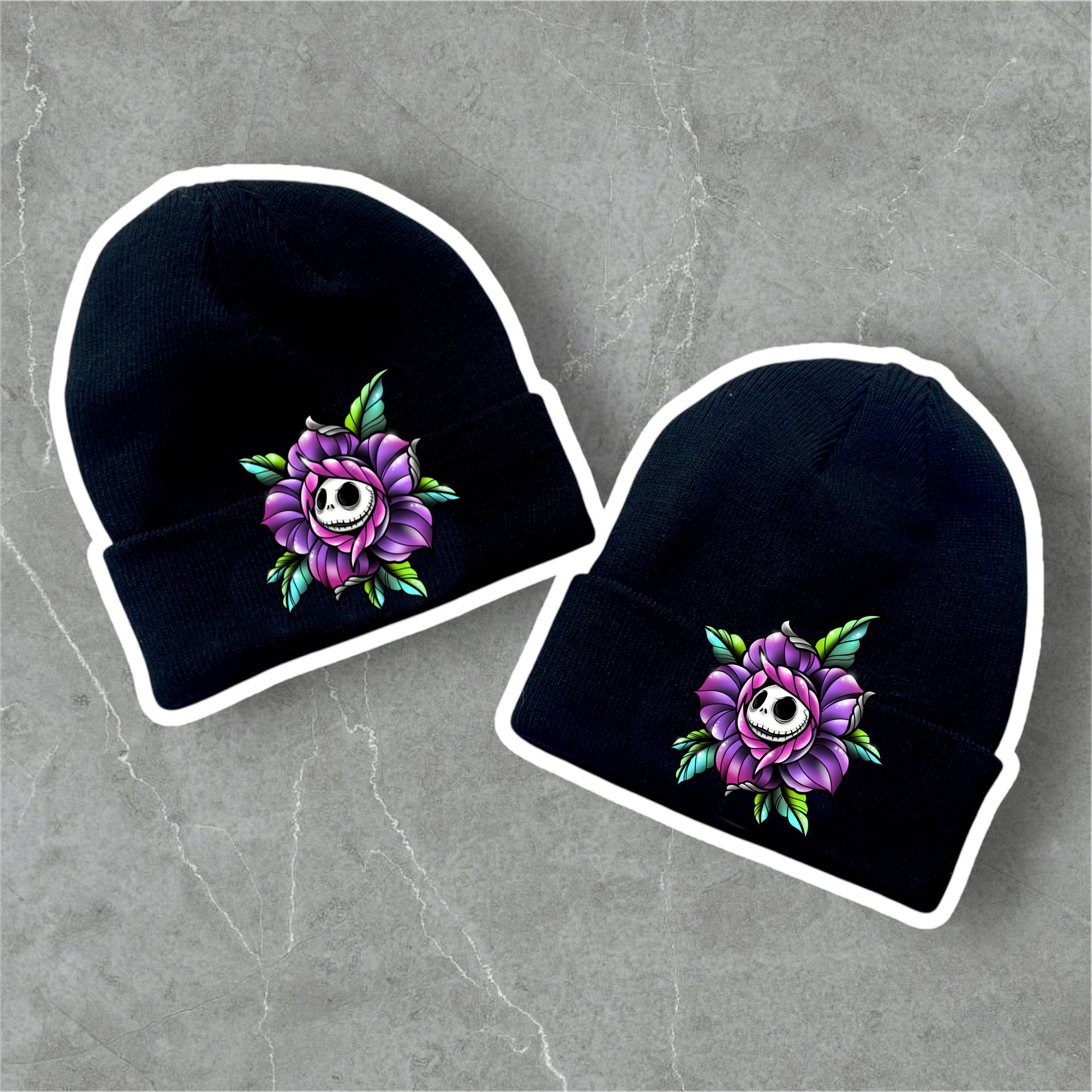 Duas gorros pretos com bordado de flor roxa e rosto de caveira no centro sobre fundo cinzento