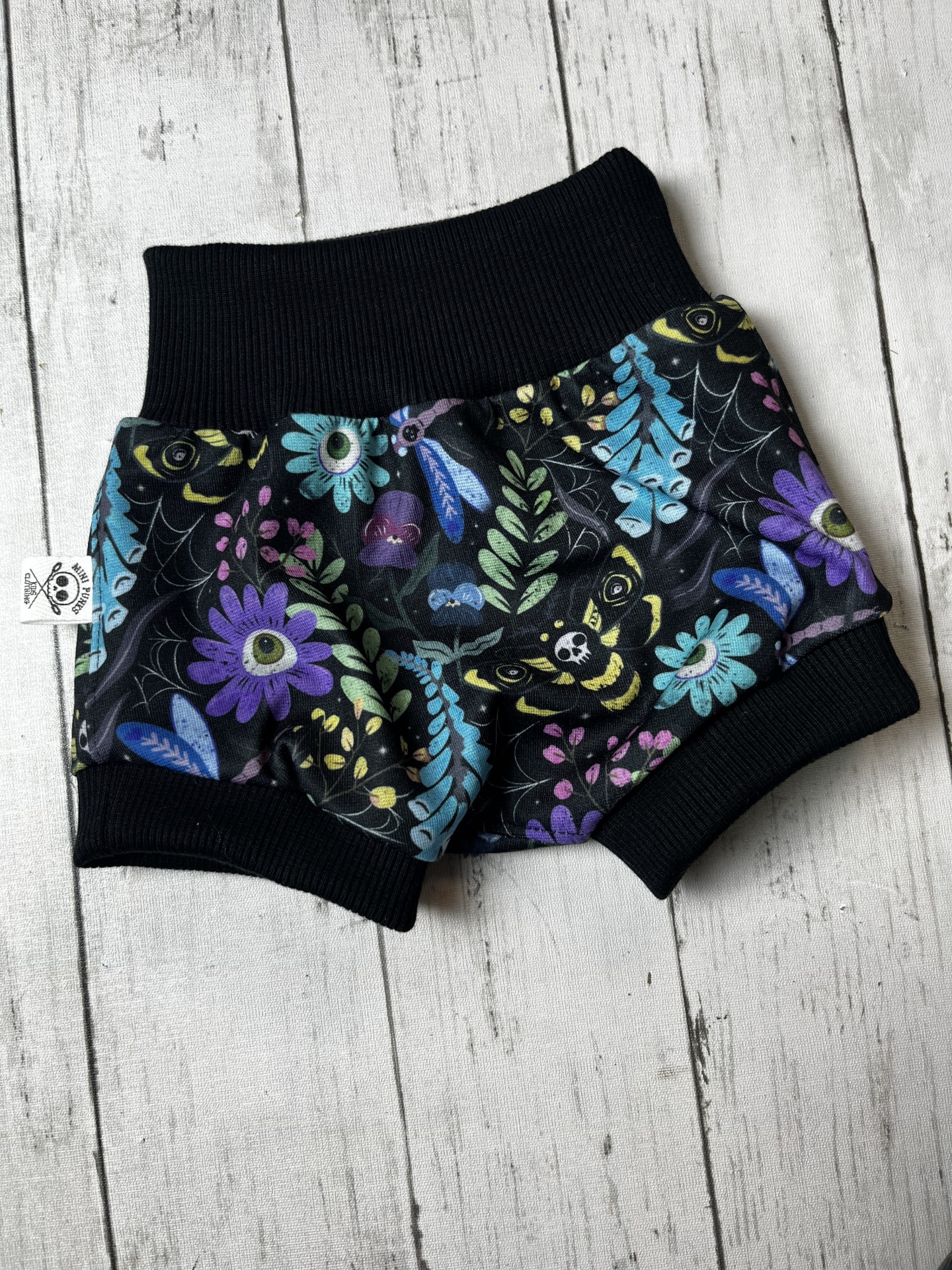 Pantalona curta para bebé com estampa floral e elementos de aranha em preto com cós e bainhas pretas