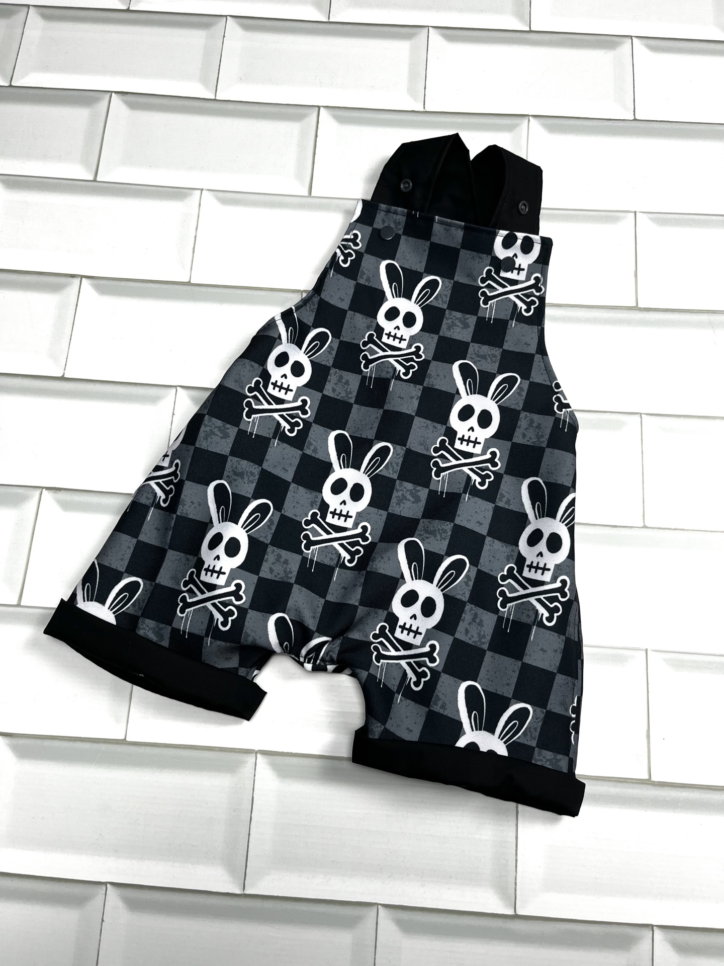 Macacão curto cinza e preto com padrão de caveiras de coelho e alças pretas