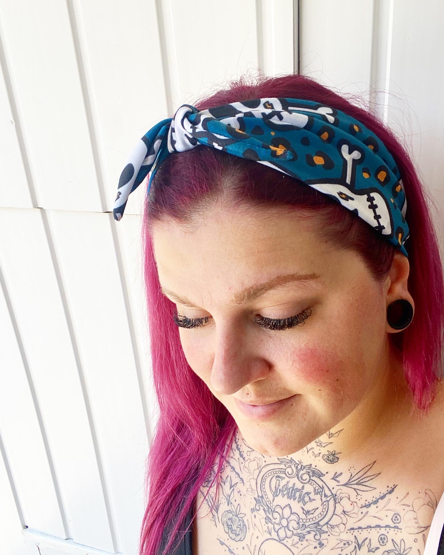 Bandana azul com padrão de ossos usada por mulher com cabelo rosa e tatuagens no peito