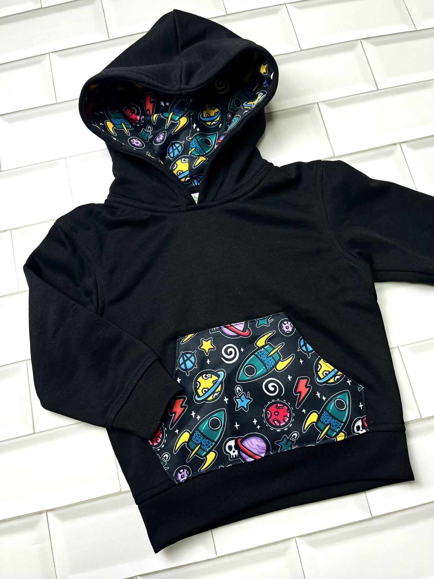 Sweatshirt preta com capuz para criança com bolso e interior do capuz com padrão de foguetes coloridos