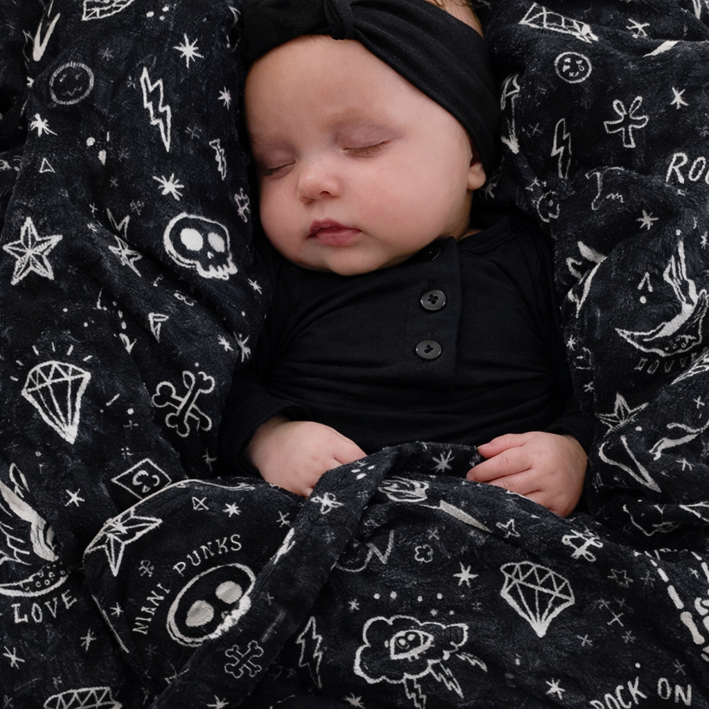 Bebé com manta preta estampada com caveiras e símbolos