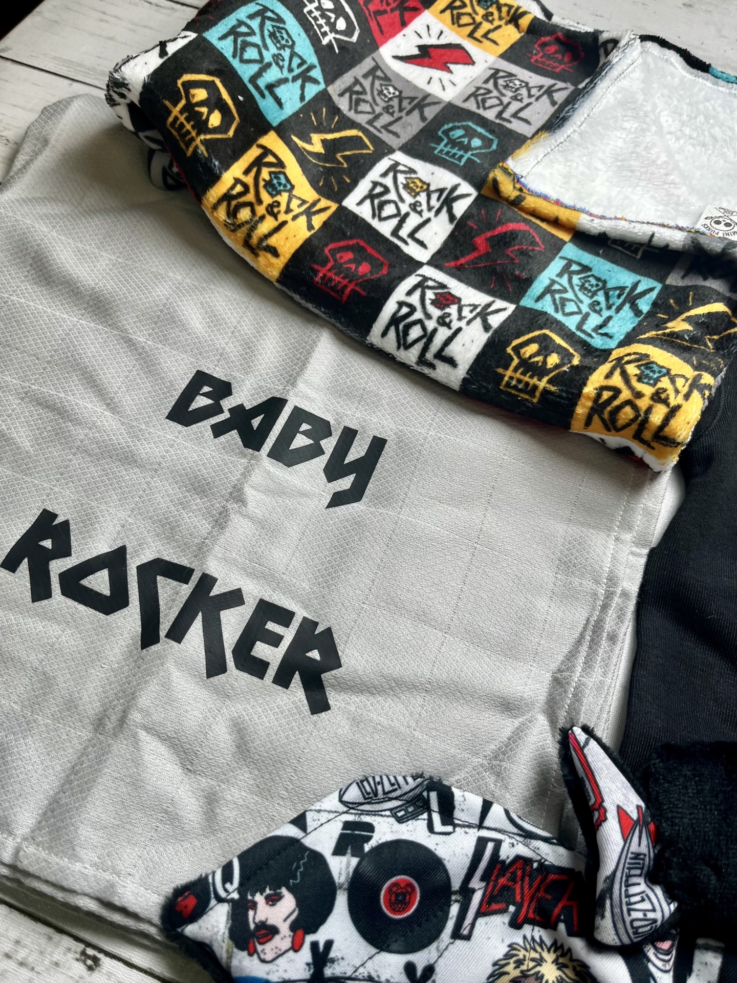Três tecidos para bebé com temas rock, cores como cinza, preto, amarelo, vermelho e azul, e padrões variados.