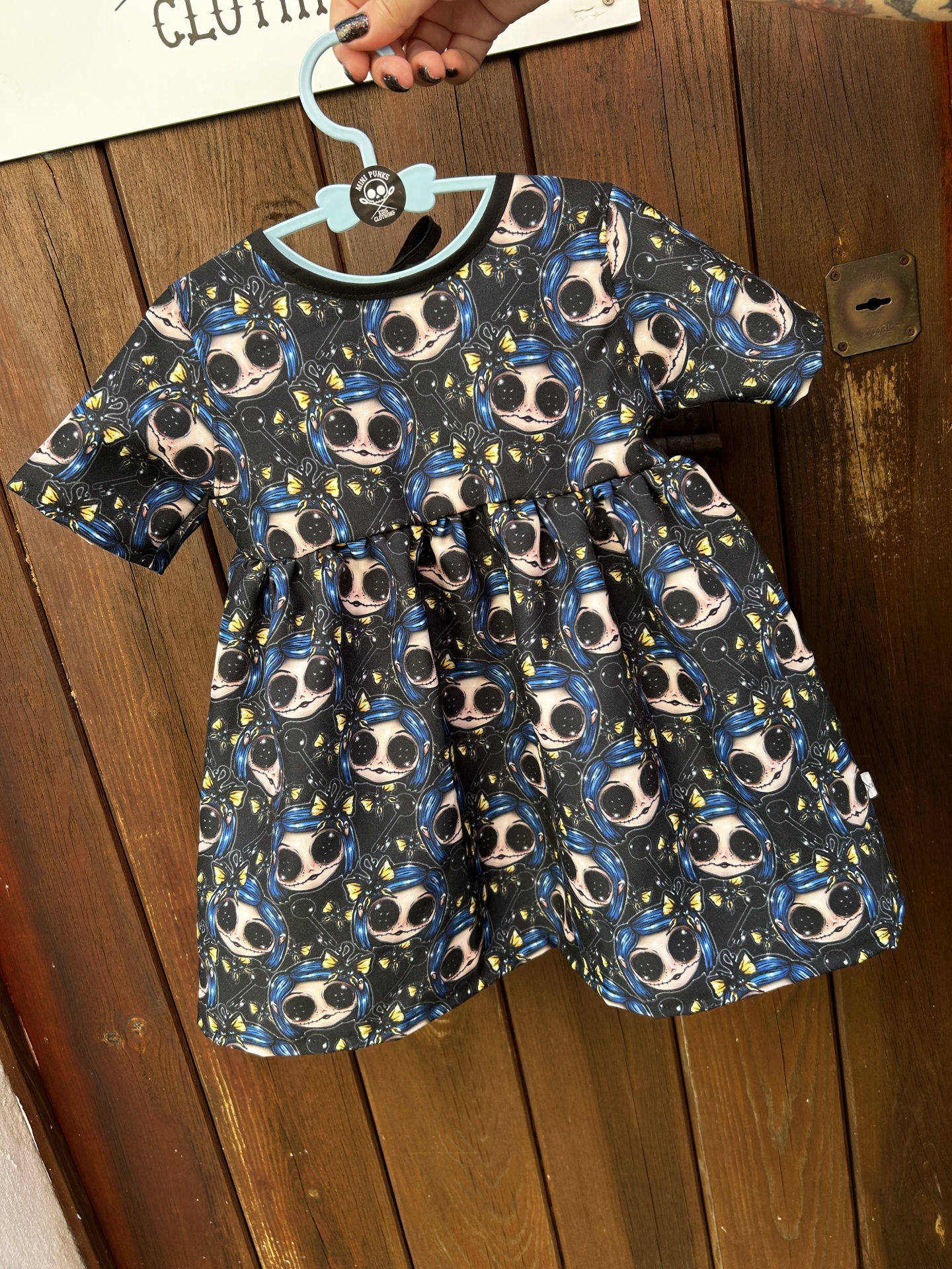 Vestido infantil colorido com padrão cartoon pendurado num cabide azul claro