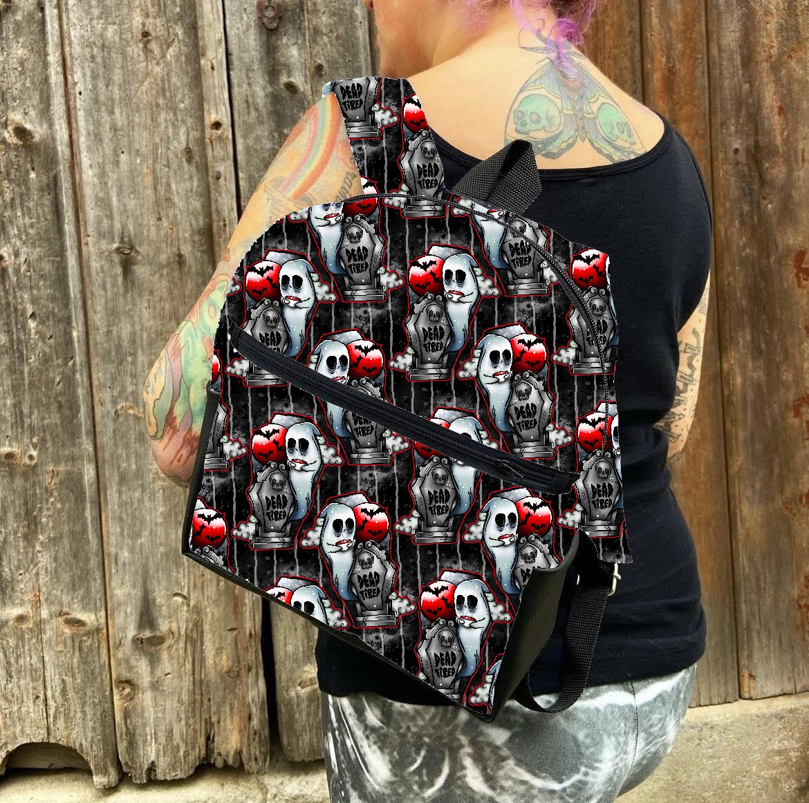 Mochila preta com padrão de caveiras e corações vermelhos fotografada numa pessoa junto a uma parede de madeira